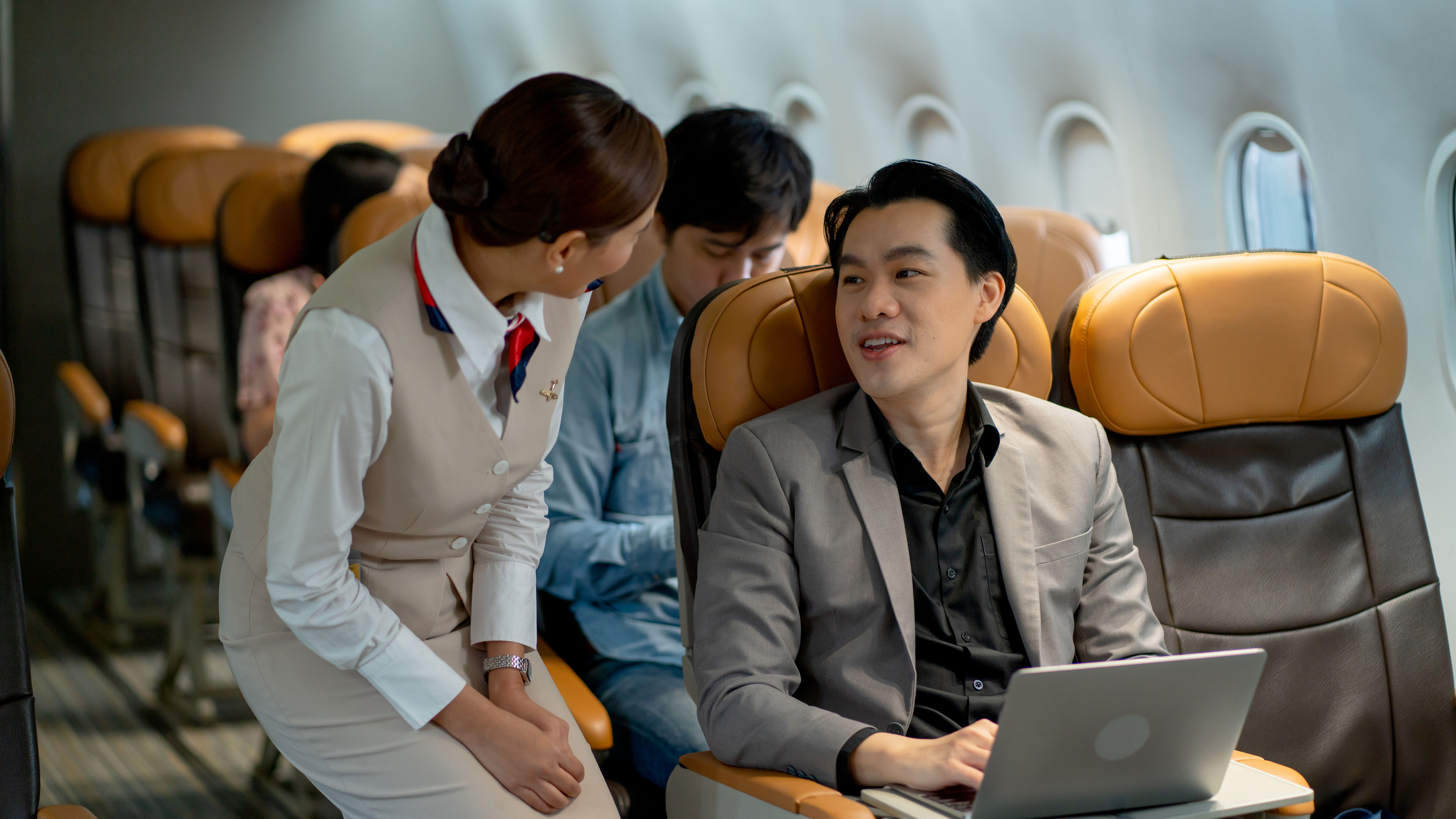 A businessman using a laptop on a plane while talking to his staff.