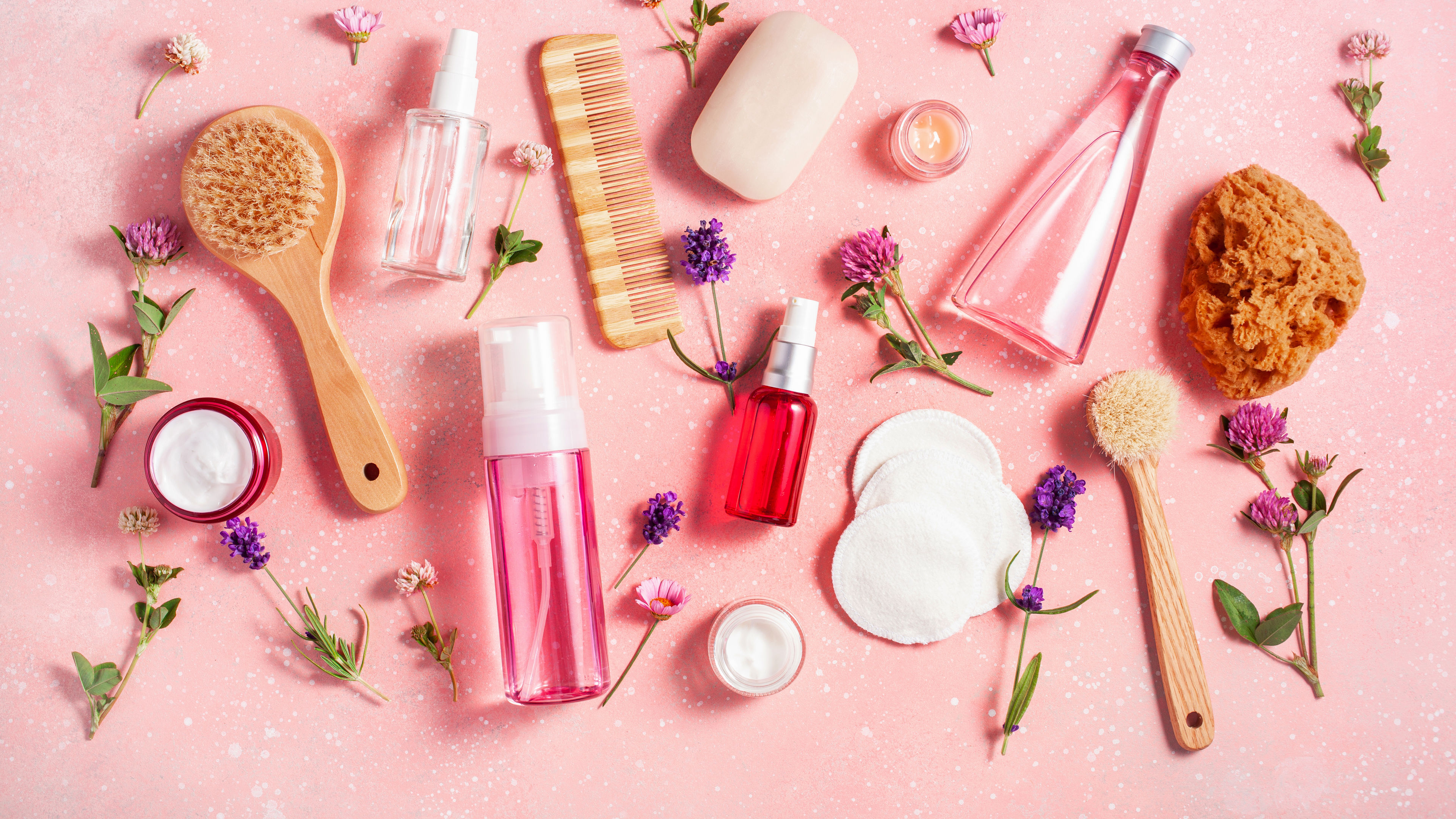 Bath at katawan pag aalaga mga produkto na may wildflowers sa isang kulay rosas na background.