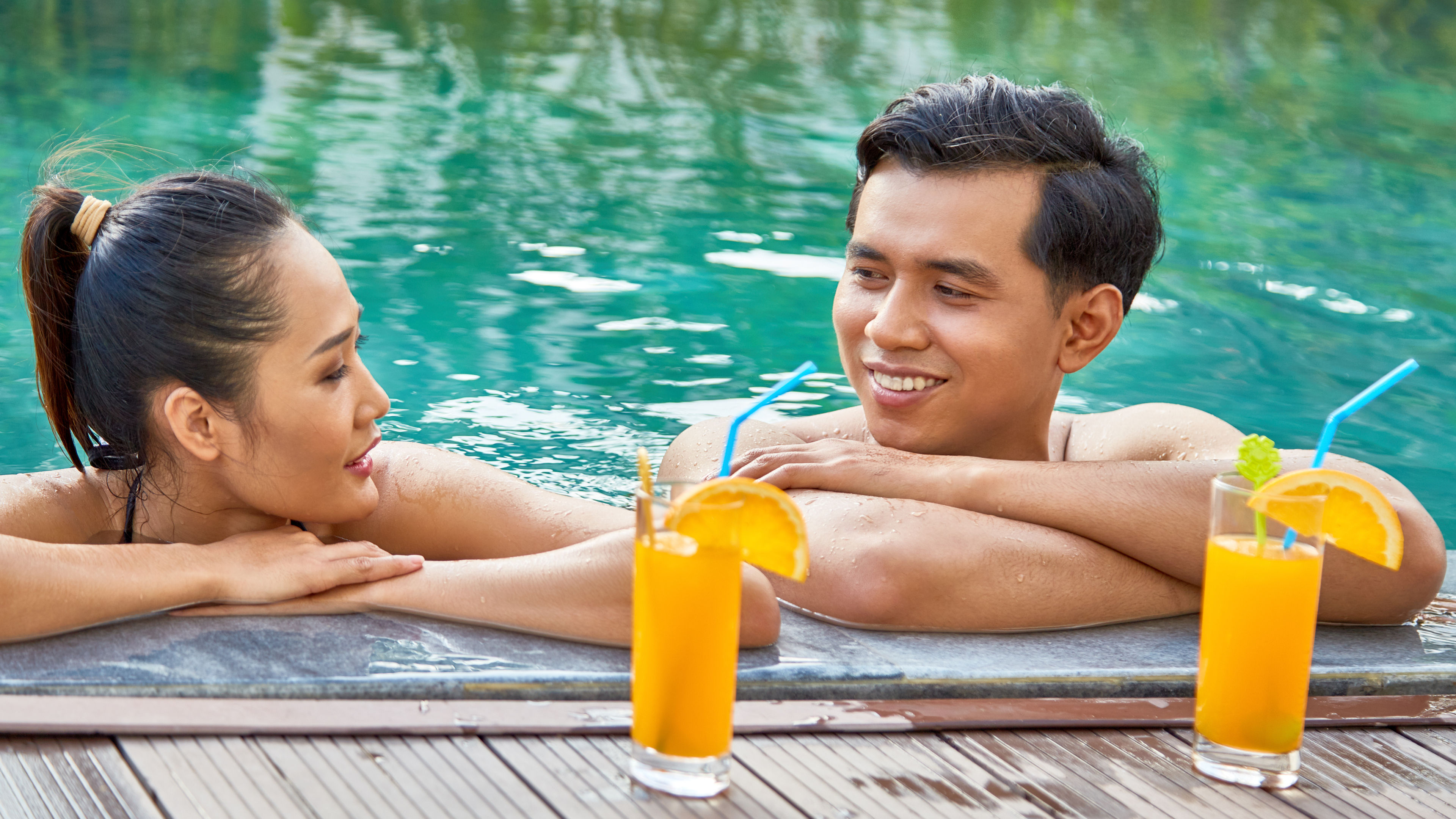 Happy Asian couple relaxing and swimming in a pool on a sunny day.