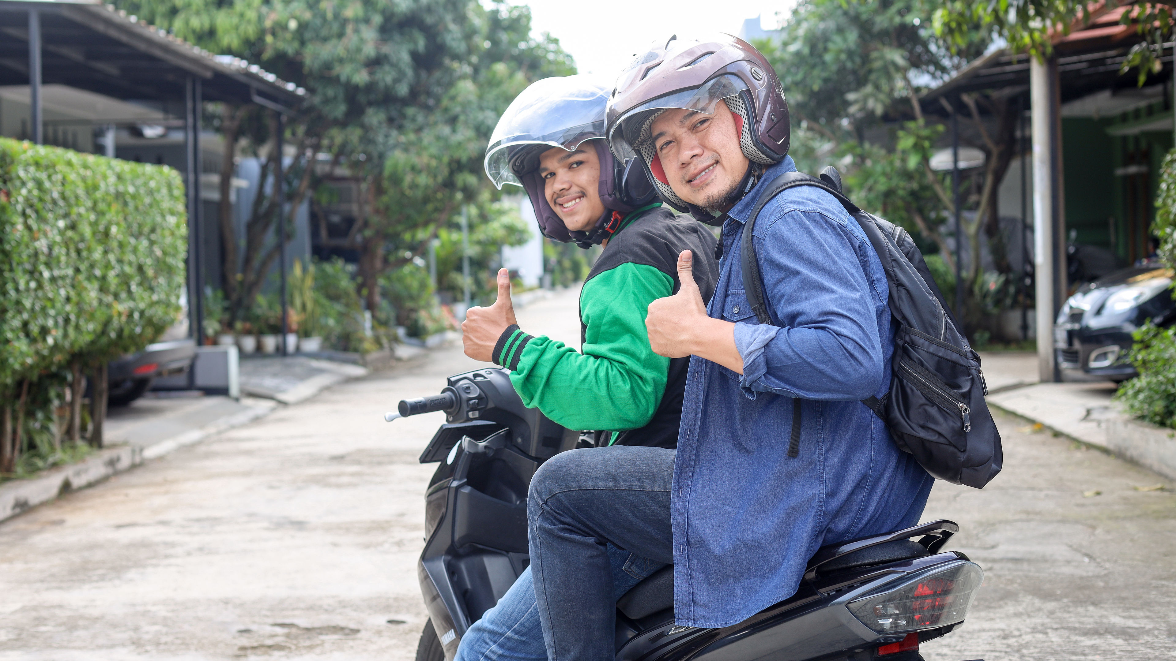 Two Filipino men on scooters, smiling and giving a thumbs-up.