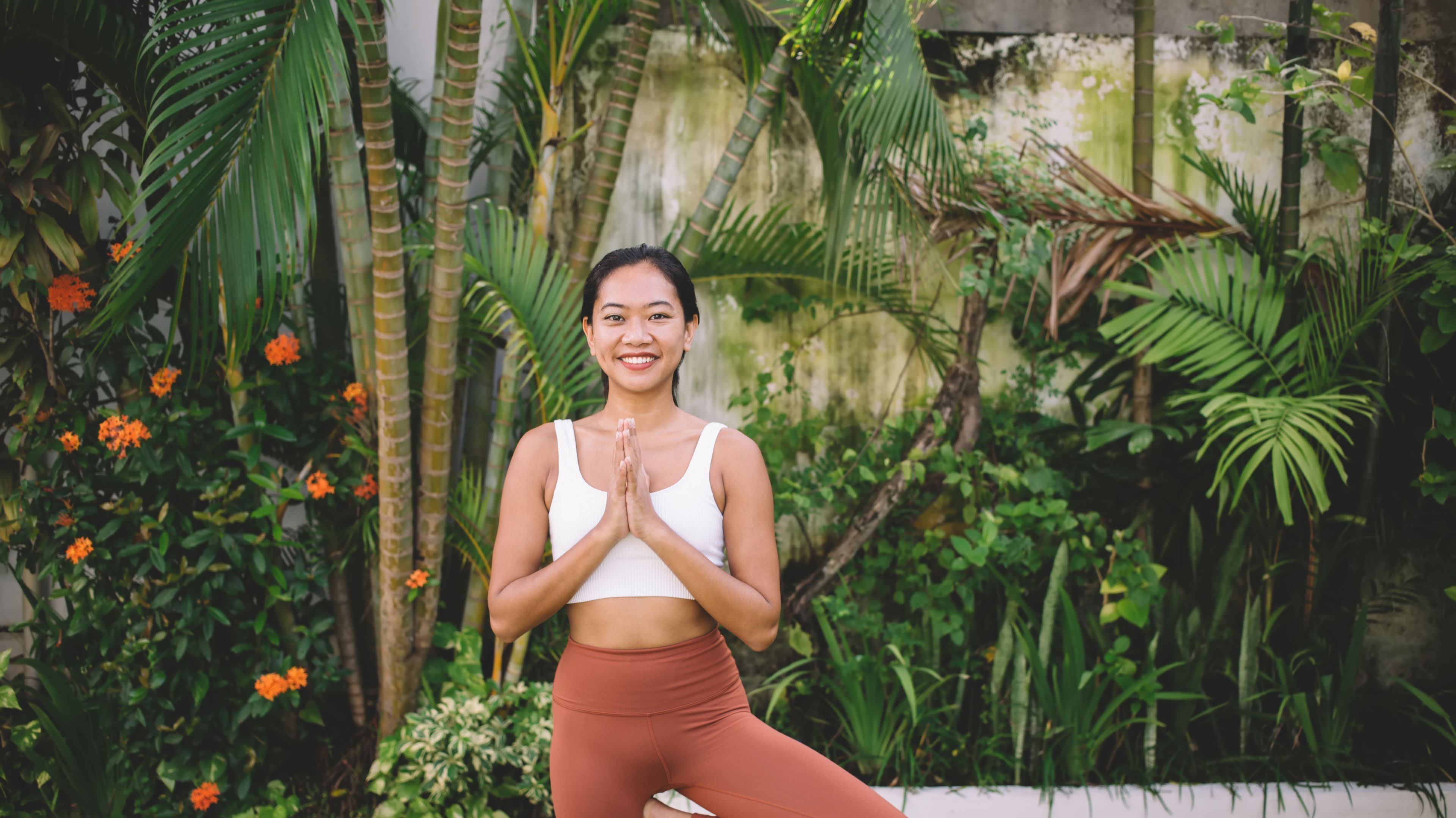 Isang babae na nakasuot ng puting crop top at kalawangin na kulay capri leggings.