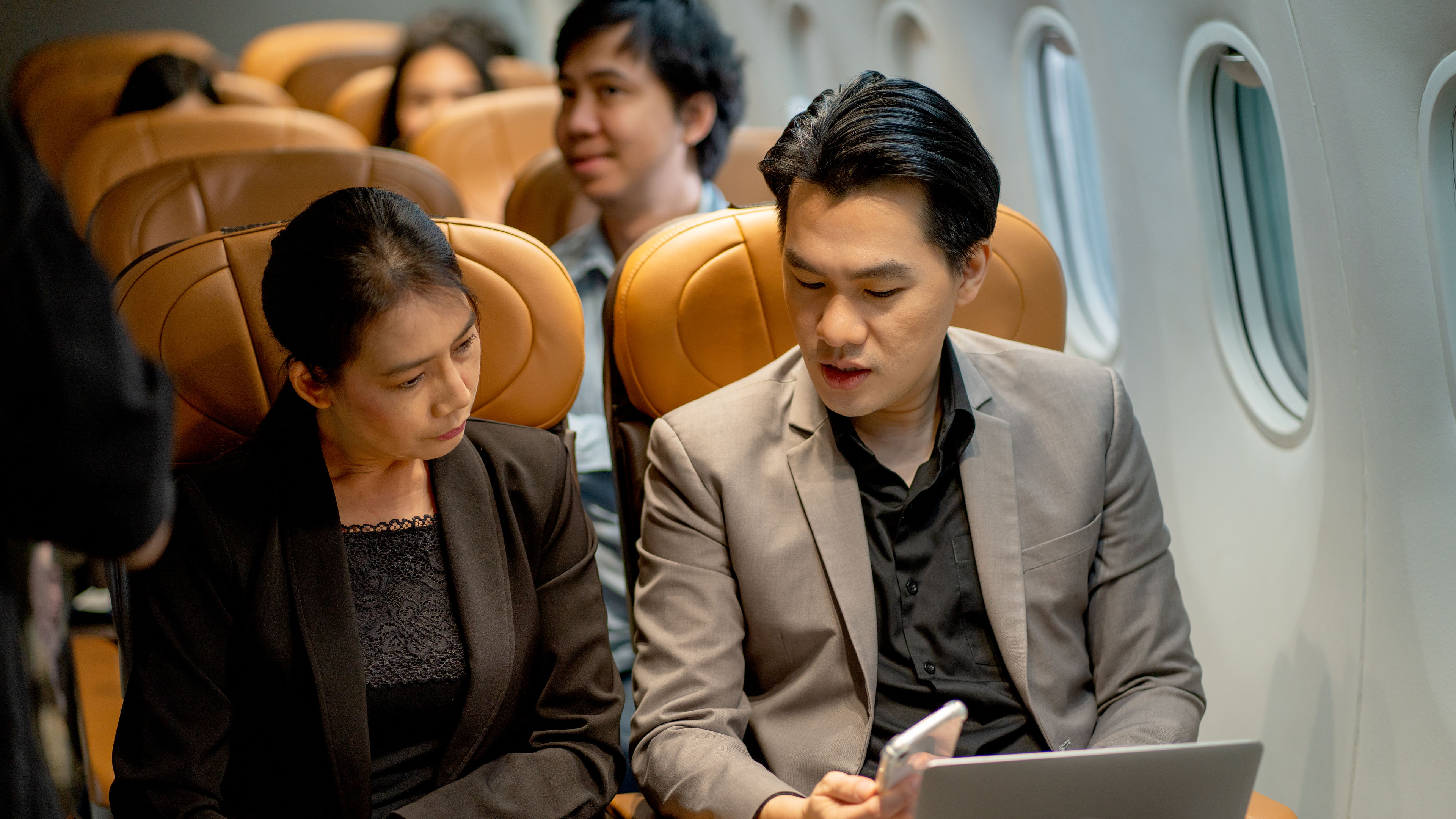 Business man use laptop and show the data in his mobile phone to co-worker during fly with airplane 