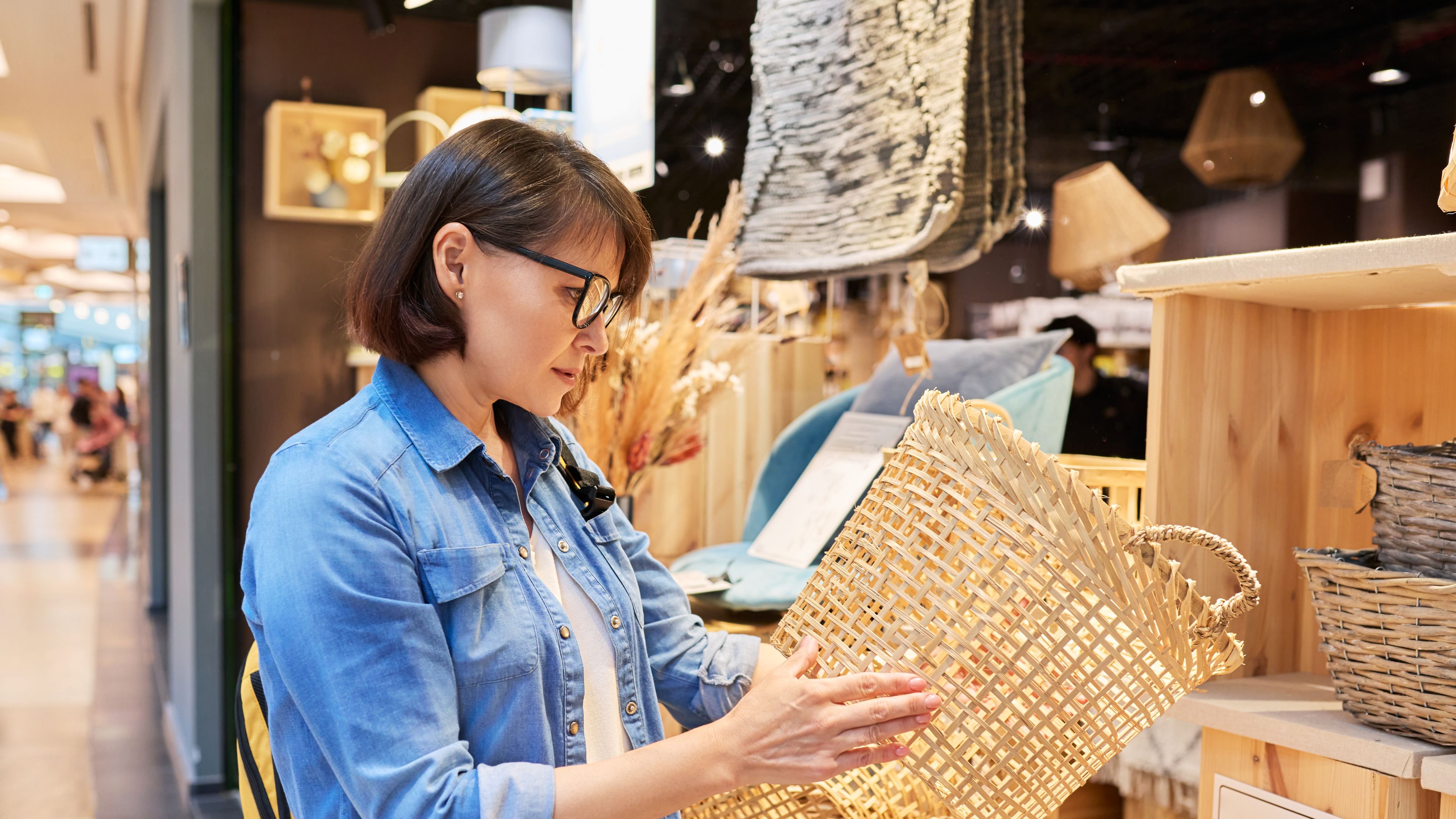 Mature woman shopper choosing interior wicker baskets in home decor store 