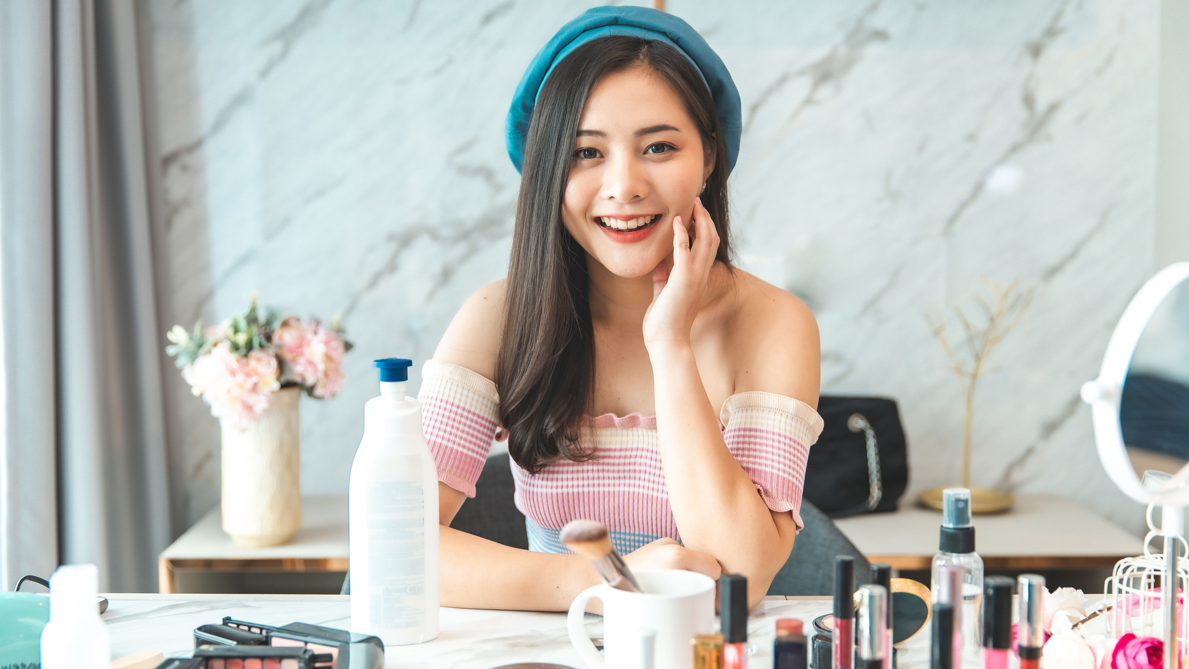 A woman smiling at a table full of makeup products on it 